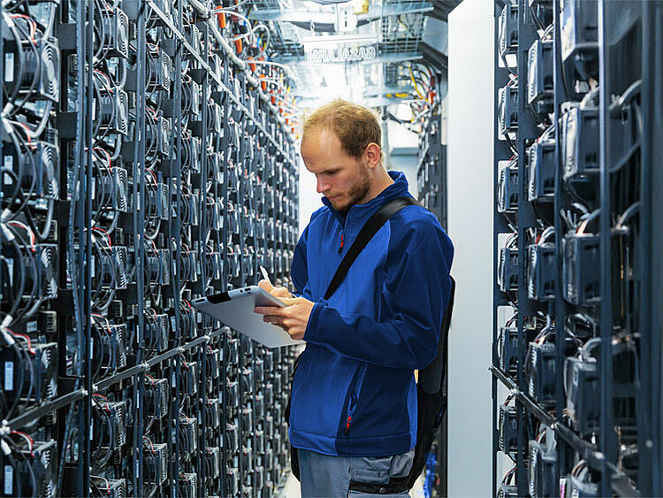 An employee stands in a large battery facility, examining data on his tablet.