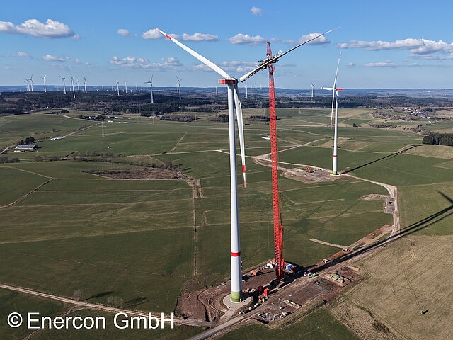 Wind turbines in a green field. In the foreground is a wind turbine with a red construction crane.