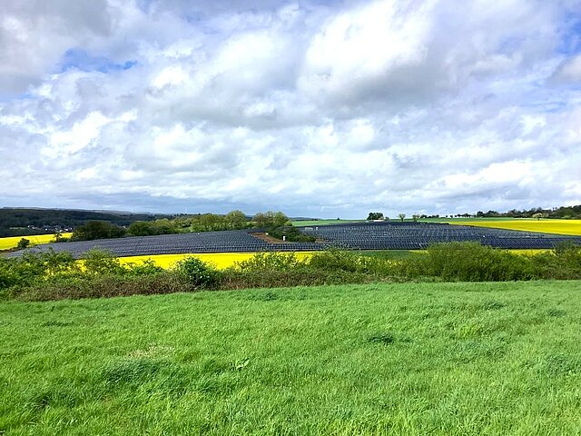 Free field solar power plant surrounded by green and yellowfields.