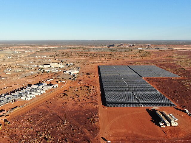 In the foreground is the solar installation for the Agnew Gold Mine in Australia. The blue panels create a strong contrast with the orange soil of the Australian outback