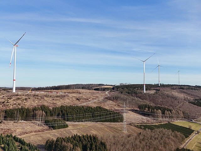 Four wind turbines stand on a hilly wooded area