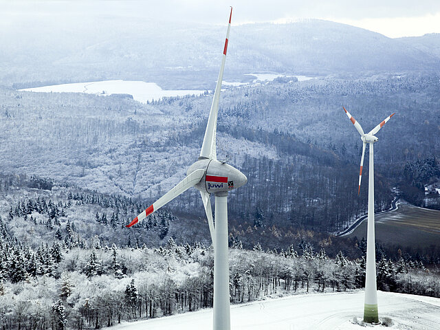 A wind turbine in winter from a bird's-eye view. The forest is covered in white snow.