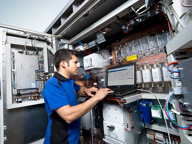 A JUWI employee is standing by a fuse box, analyzing data on his laptop.