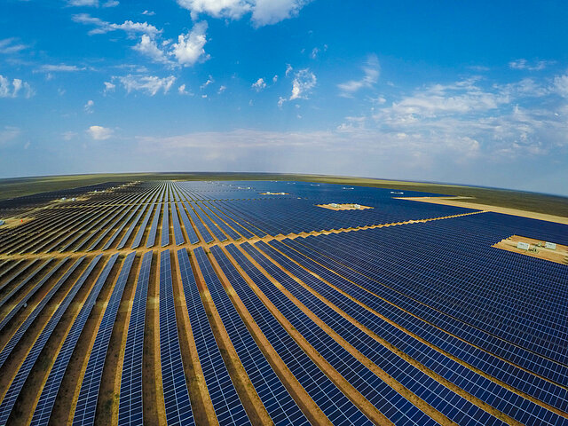 The image shows a large solar park. It extends almost to the horizon. The sun is shining on the panels.