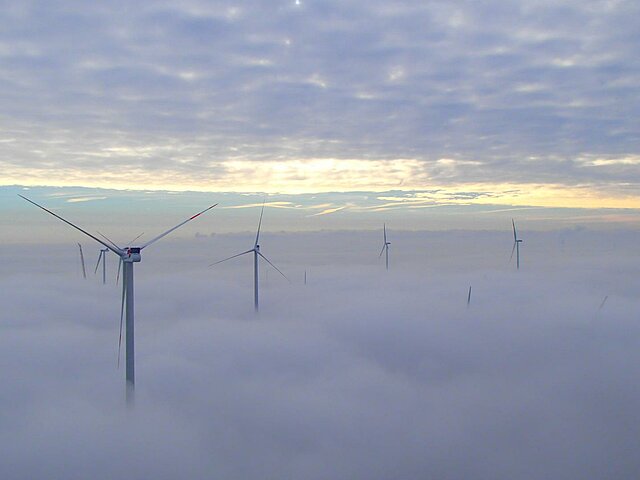 A wind turbine rises above a thick cloud cover.