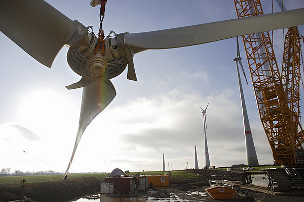A construction crane lifts the blades of a wind turbine.