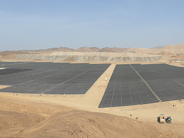 Solar park at the mine in Egypt. In the background, mountains and debris piles are visible. The sun is shining on the long rows of black photovoltaic panels.