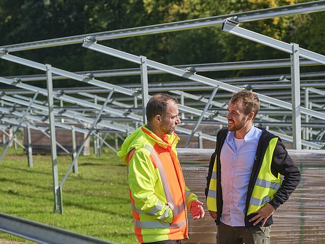 Two JUWI colleagues stand in front of the solar park under construction and discuss with each other.